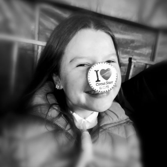 "An image of a little girl smiling, she has an I love circus starr sticker on her nose."